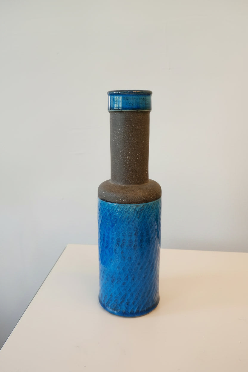 Blue cylindrical object with textured surface and brown handle, measured by a yellow ruler on a white background.