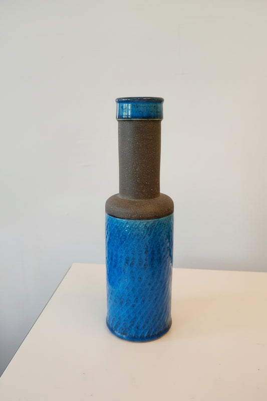 Blue cylindrical object with textured surface and brown handle, measured by a yellow ruler on a white background.