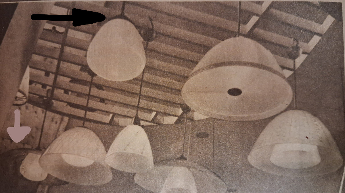 A vintage black-and-white photograph showing multiple pendant light shades hanging from a slatted ceiling in an interior room. From 1946.