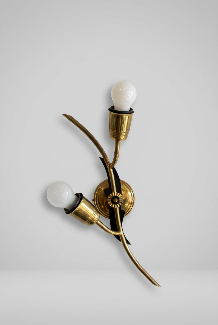 A modern wall-mounted light fixture with two curved brass arms, black accents, and two frosted glass bulbs against a plain white wall.