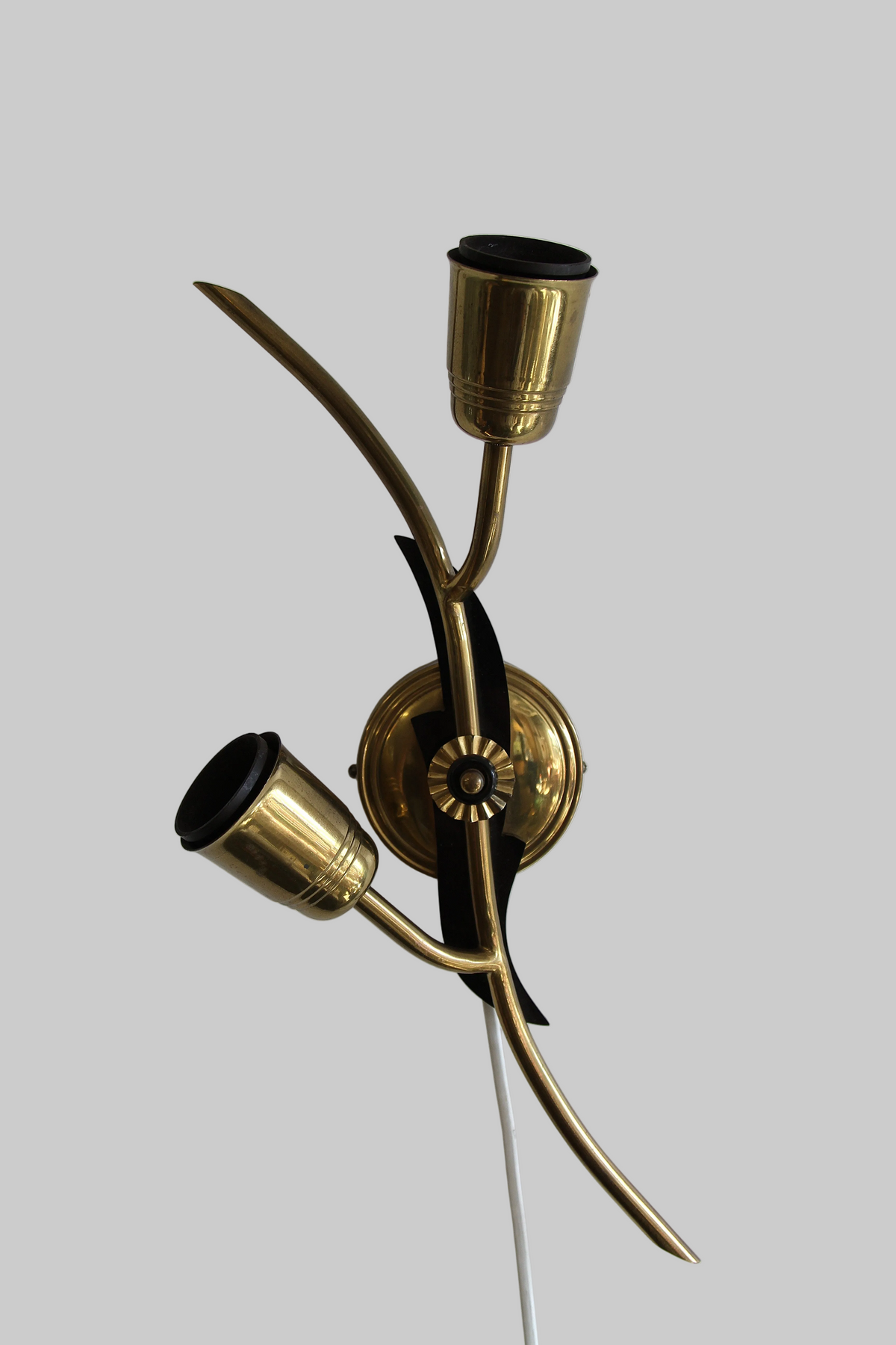 A mid-century modern brass wall sconce with two curved arms and black accents, mounted on a white wall.