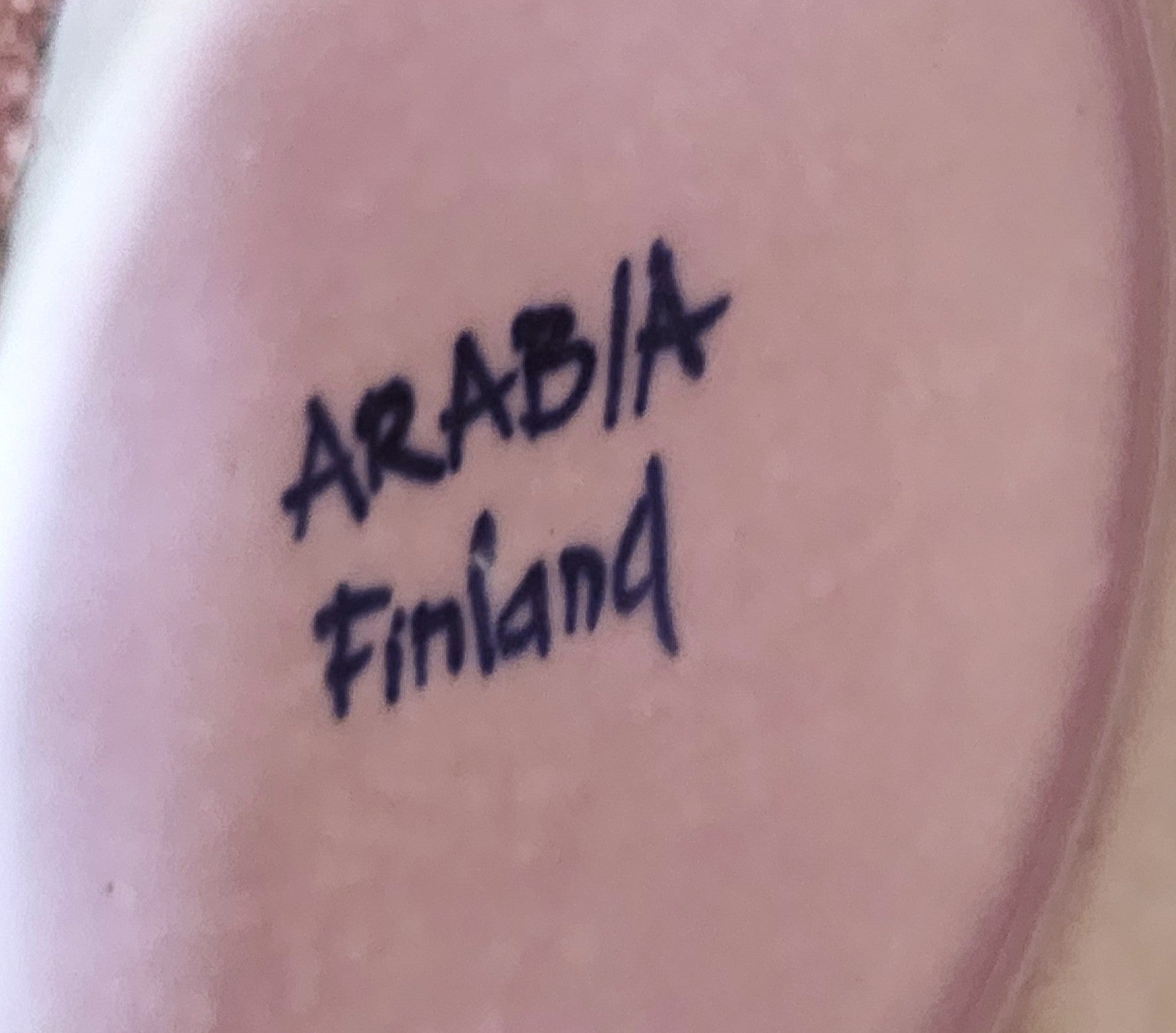 Text 'ARABIA Finland' on a ceramic plate with a pinkish hue.