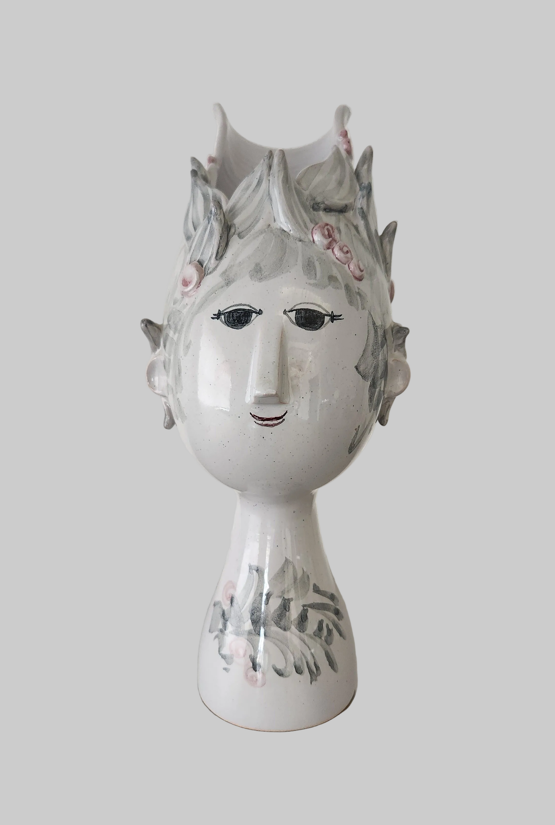 Decorative ceramic head with painted face and floral crown on a plain background