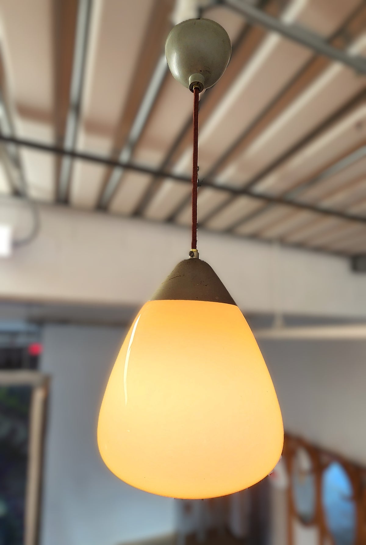 A vintage Orno pendant light with a glowing warm yellow glass shade, a dark metal collar, and a dark cord hanging from a ceiling fixture in an indoor setting.