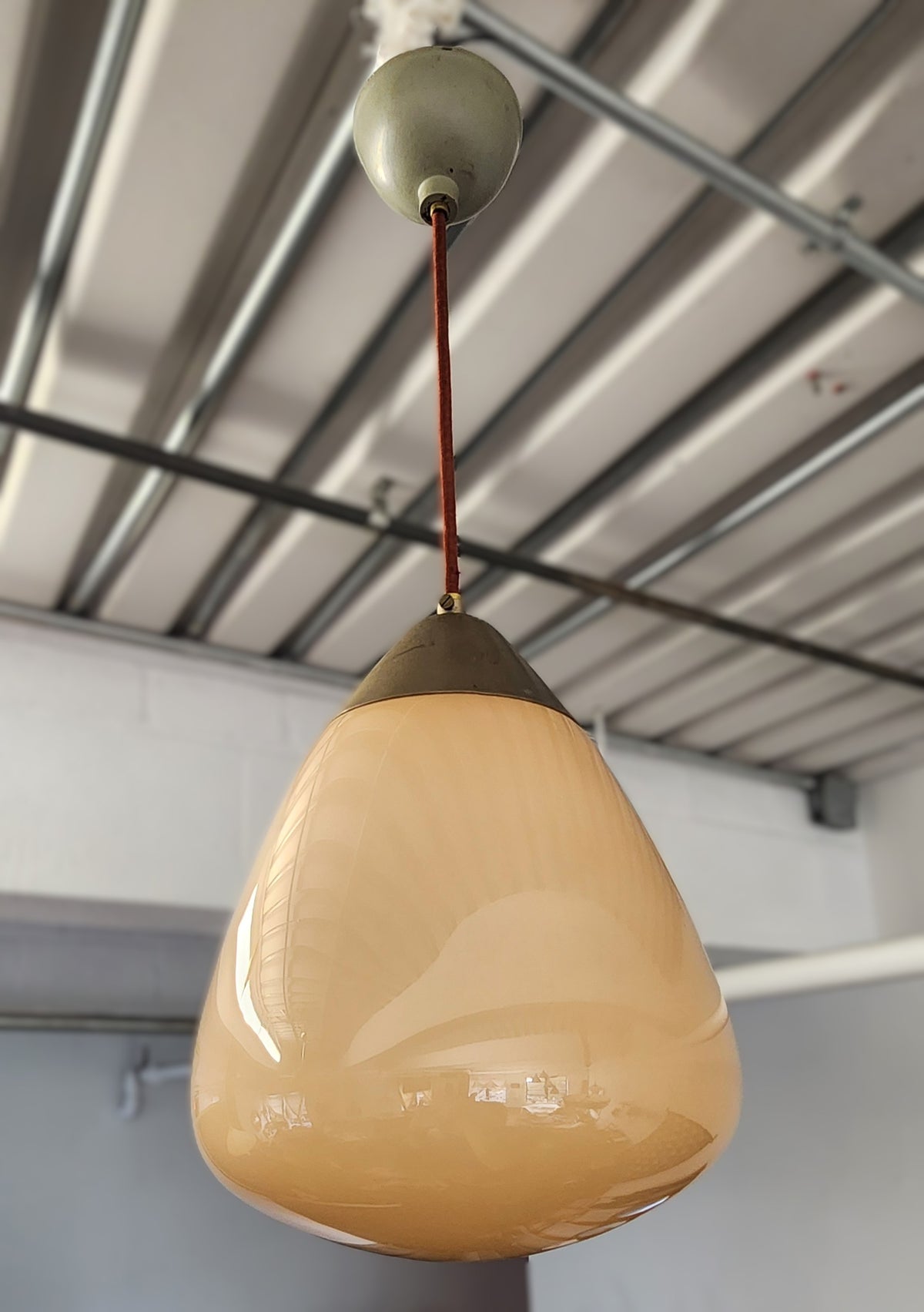 A vintage Orno pendant light with a teardrop-shaped frosted glass shade in a warm beige color, hanging from a dark metal cap and a brown cord against an industrial ceiling.