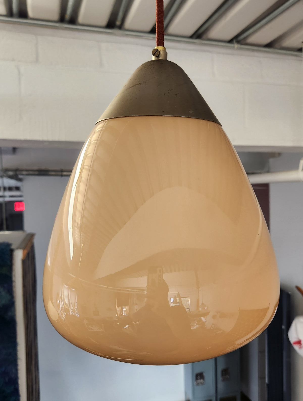 A vintage Orno drop shaped pendant light with a warm taupe glass shade and a dark metal top cap, hanging from a brown cord in an indoor warehouse or showroom setting.