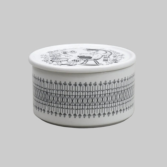 A round white ceramic lidded box made by Arabia, with black printed patterns, including a decorative border and a portrait illustration on the lid of a woman with a fat cat on her lap, set against a neutral gray background. 