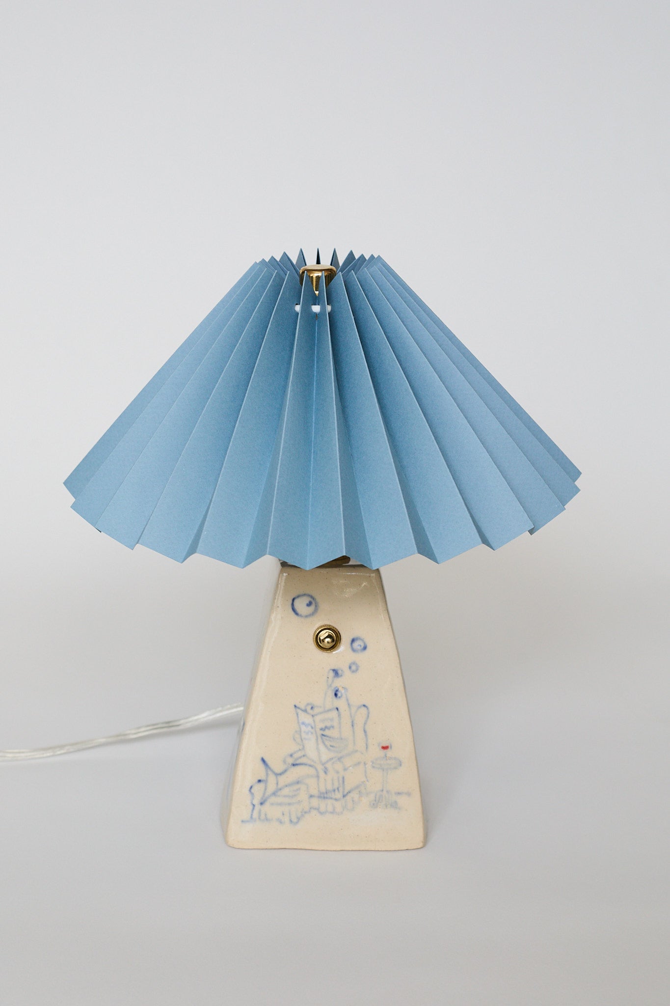 handmade ceramic table lamp with blue pleated shade and base with hand-drawn illustration of a Fish Dad lounging