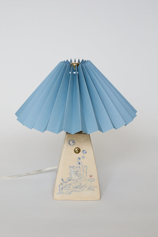 handmade ceramic table lamp with blue pleated shade and base with hand-drawn illustration of a Fish Dad lounging