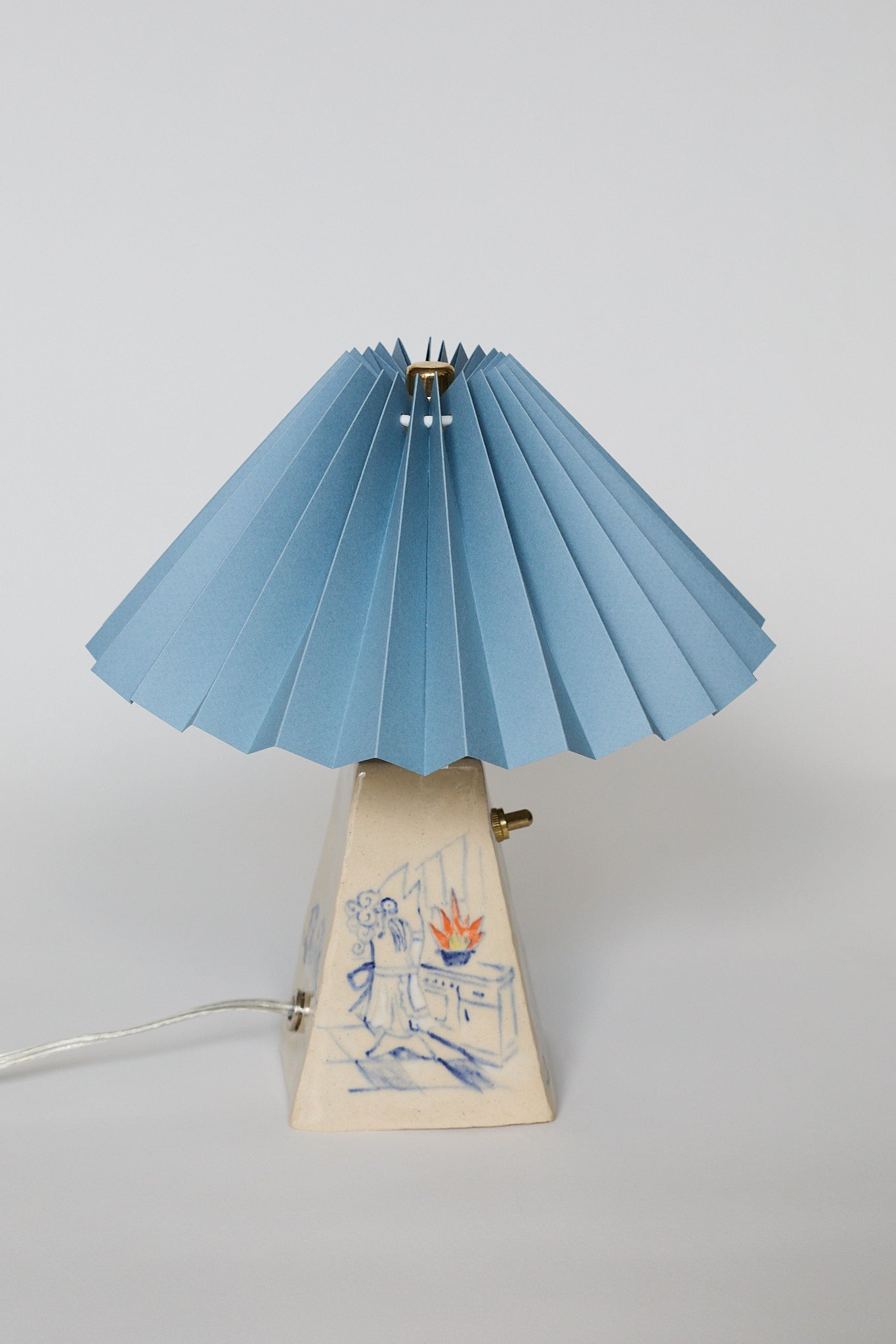 handmade ceramic table lamp with blue pleated shade and base with hand-drawn illustration of a Fish Wife cooking
