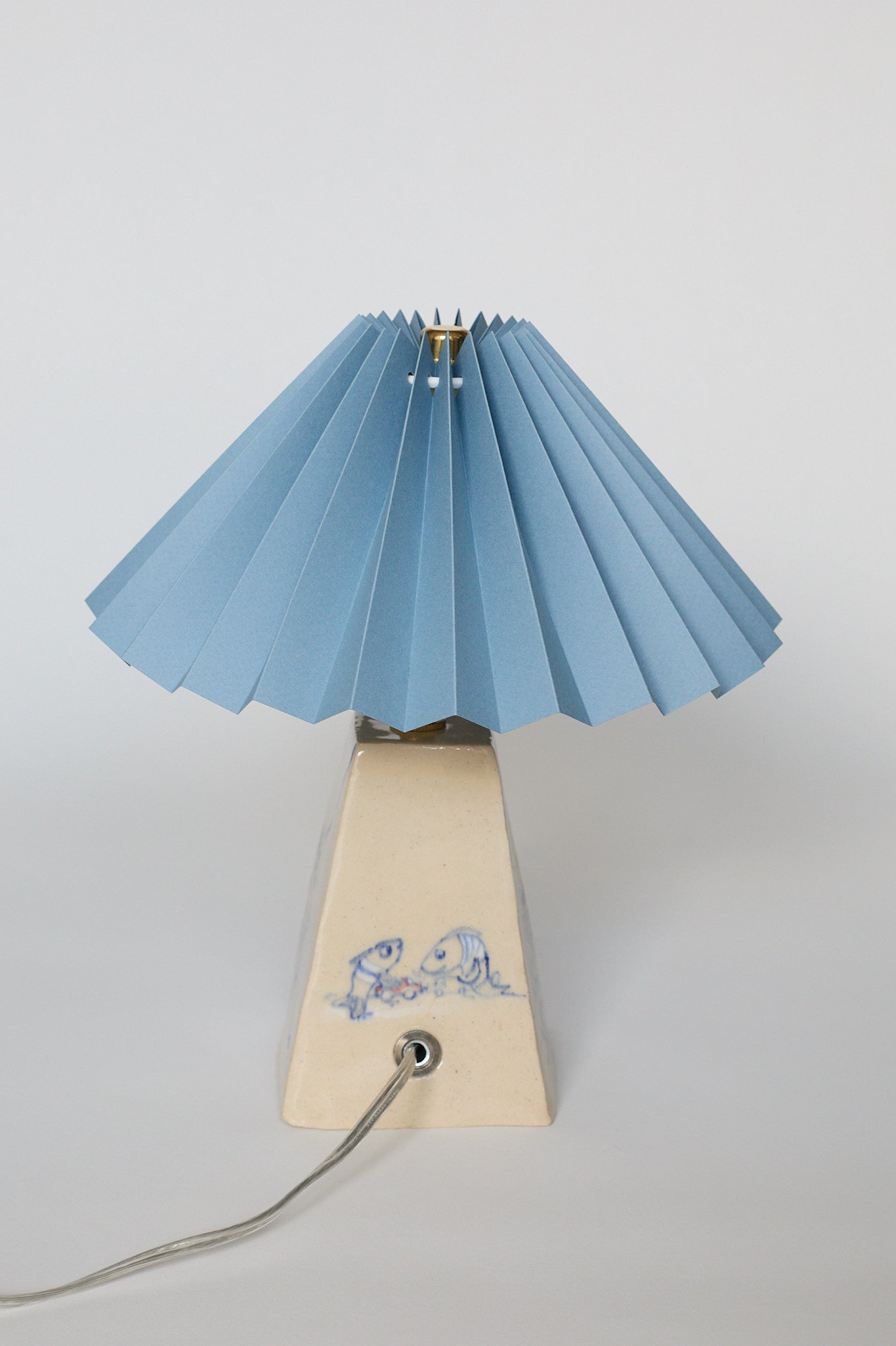 handmade ceramic table lamp with blue pleated shade and base with hand-drawn illustration of 2 little fish playing