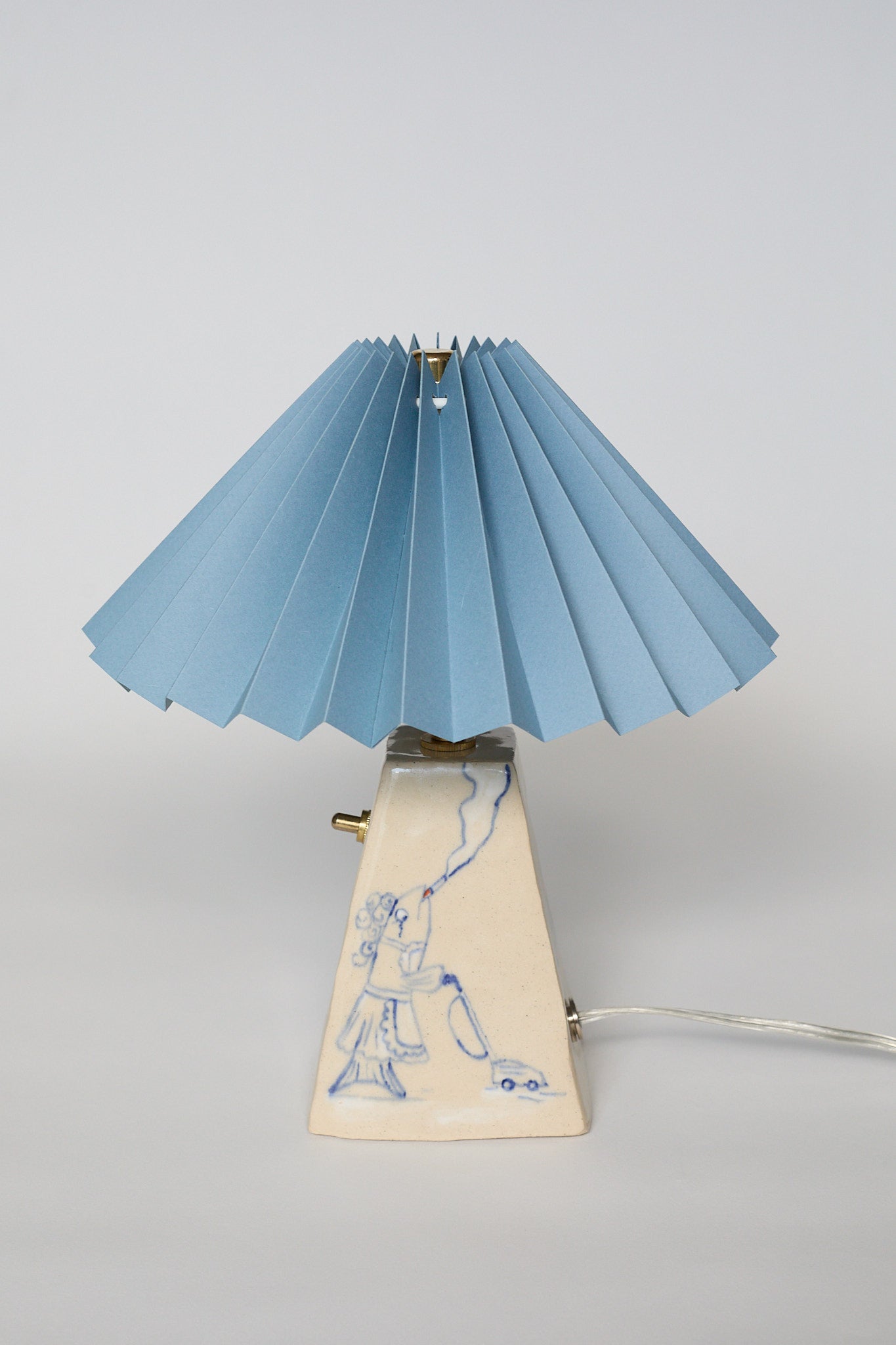 handmade ceramic table lamp with blue pleated shade and base with hand-drawn illustration of a Fish Wife vacuuming