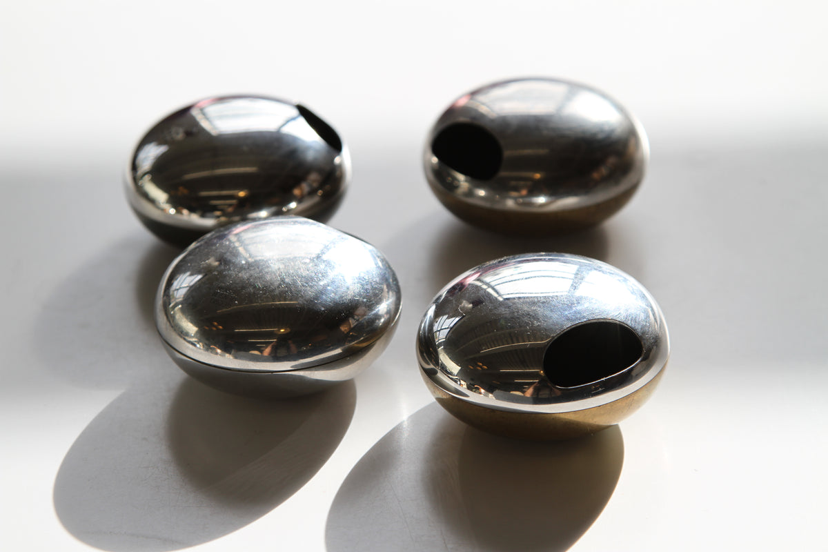 Four polished metallic dome-shaped objects with circular cutouts, arranged on a white surface with strong sunlight and shadows.