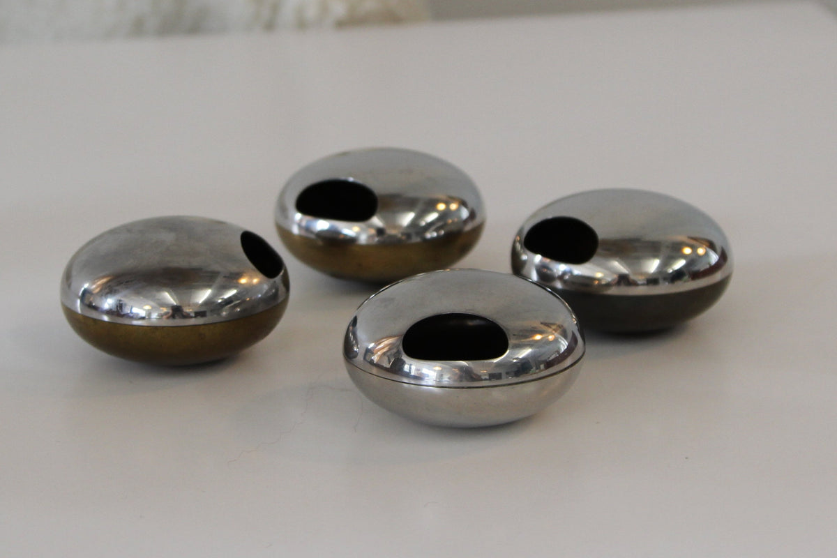 Four small metallic dome-shaped objects with circular cutouts, arranged on a white tabletop in a softly lit indoor setting.