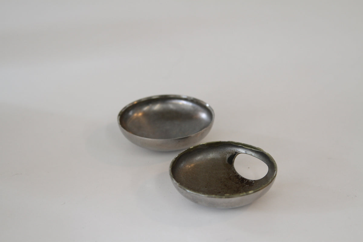 Two small oval metal dish-like containers with a cutout, shown on a plain light background.