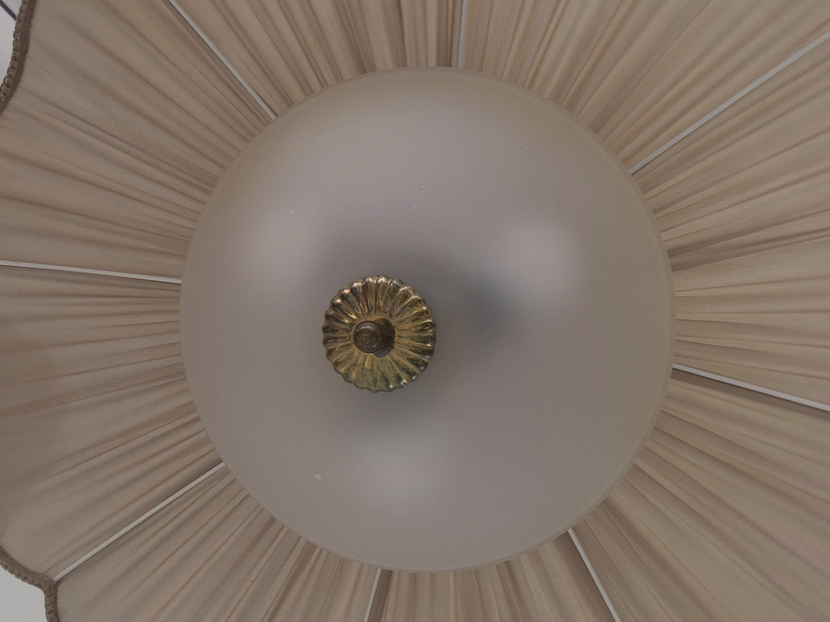 A close-up overhead view of a light fixture with a large frosted white globe shade and a central gold-toned decorative finial, and a taupe pleated fabric shade