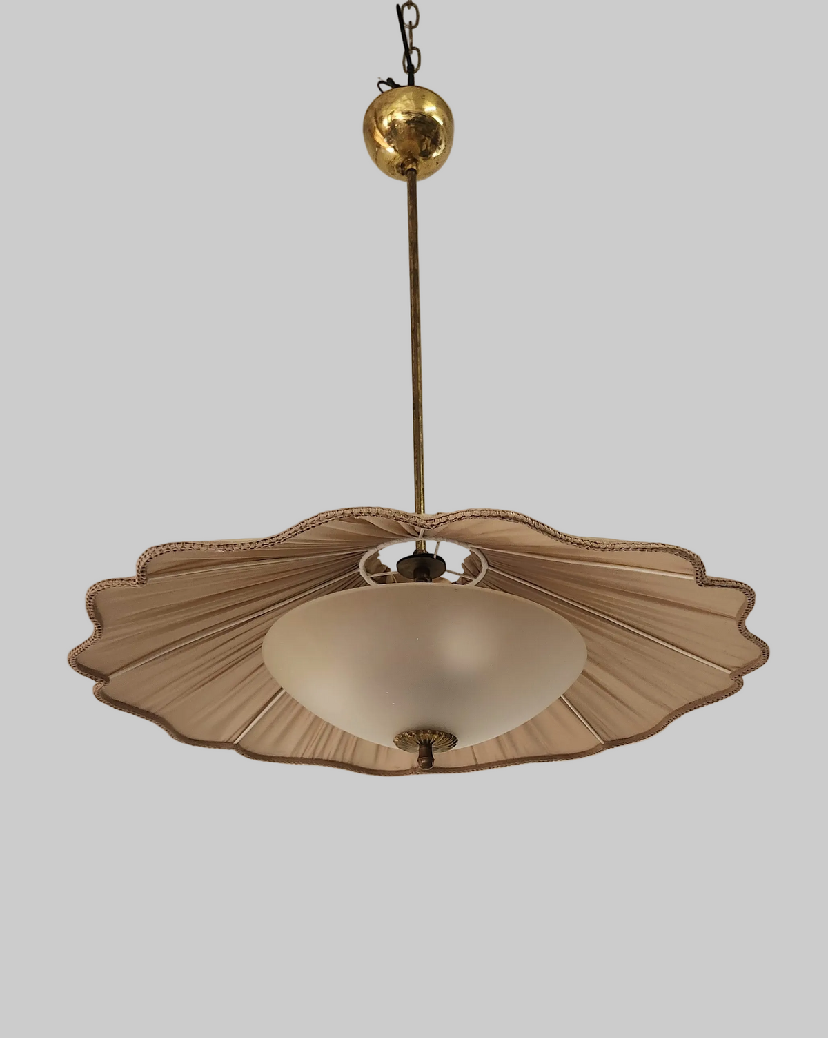 A vintage mid-century modern pendant light with a pleated beige fabric shade, a central frosted glass bowl, and a brass suspension rod and globe.