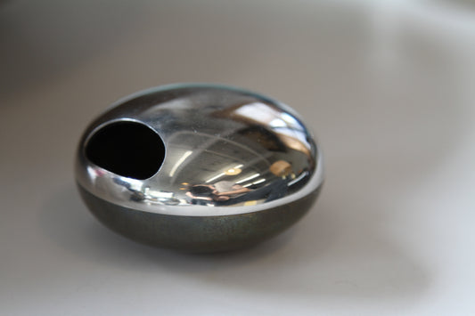 A polished chrome oval soap dish with a circular cutout, resting on a neutral surface. Top is polished silver, base is bronze.