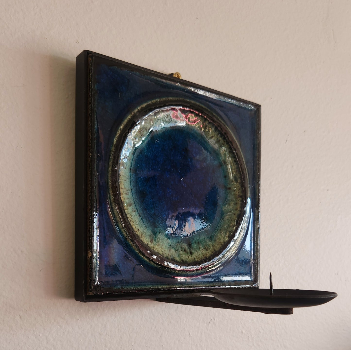 Decorative wall piece with a circular blue and green ceramic element on a beige wall.