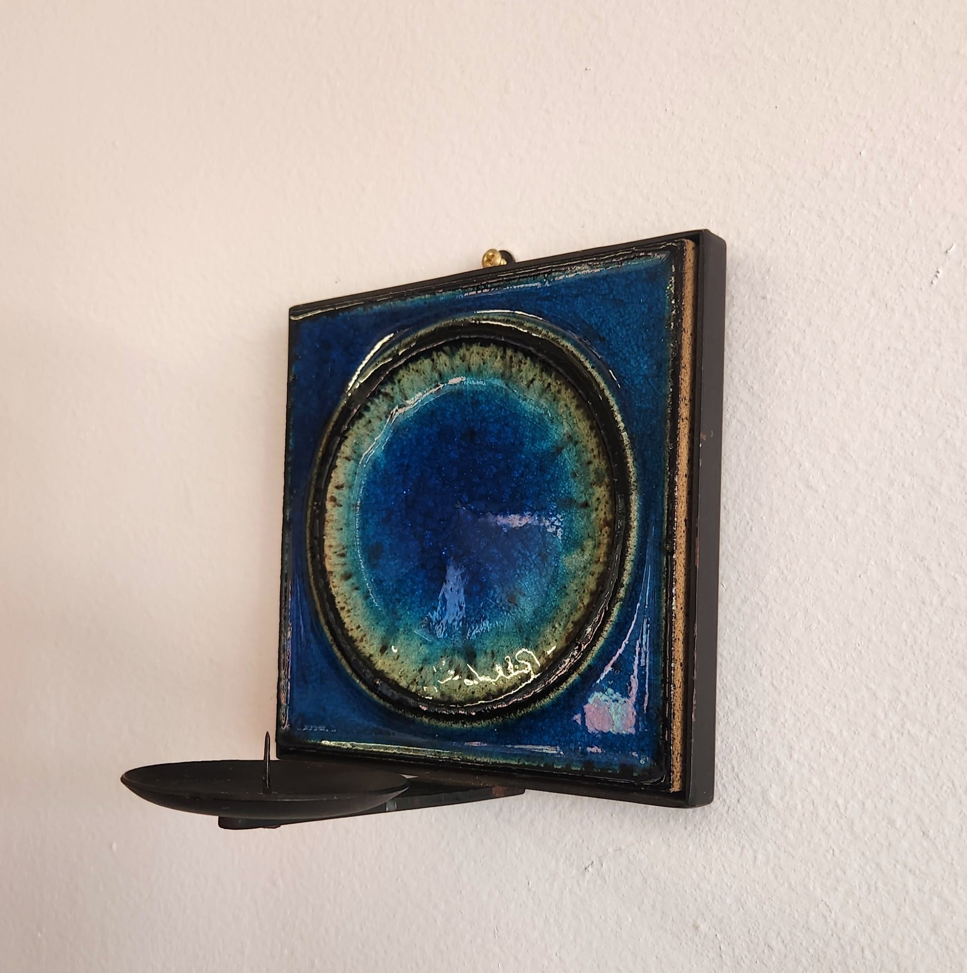 Decorative wall shelf with a blue and gold circular design on a white wall.