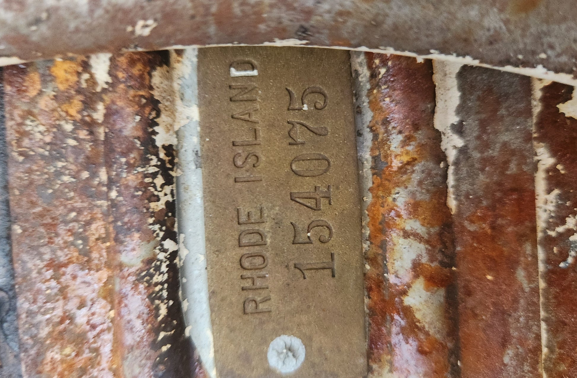 Rust-covered metal plate with 'Rhode Island 154075' text on a textured background