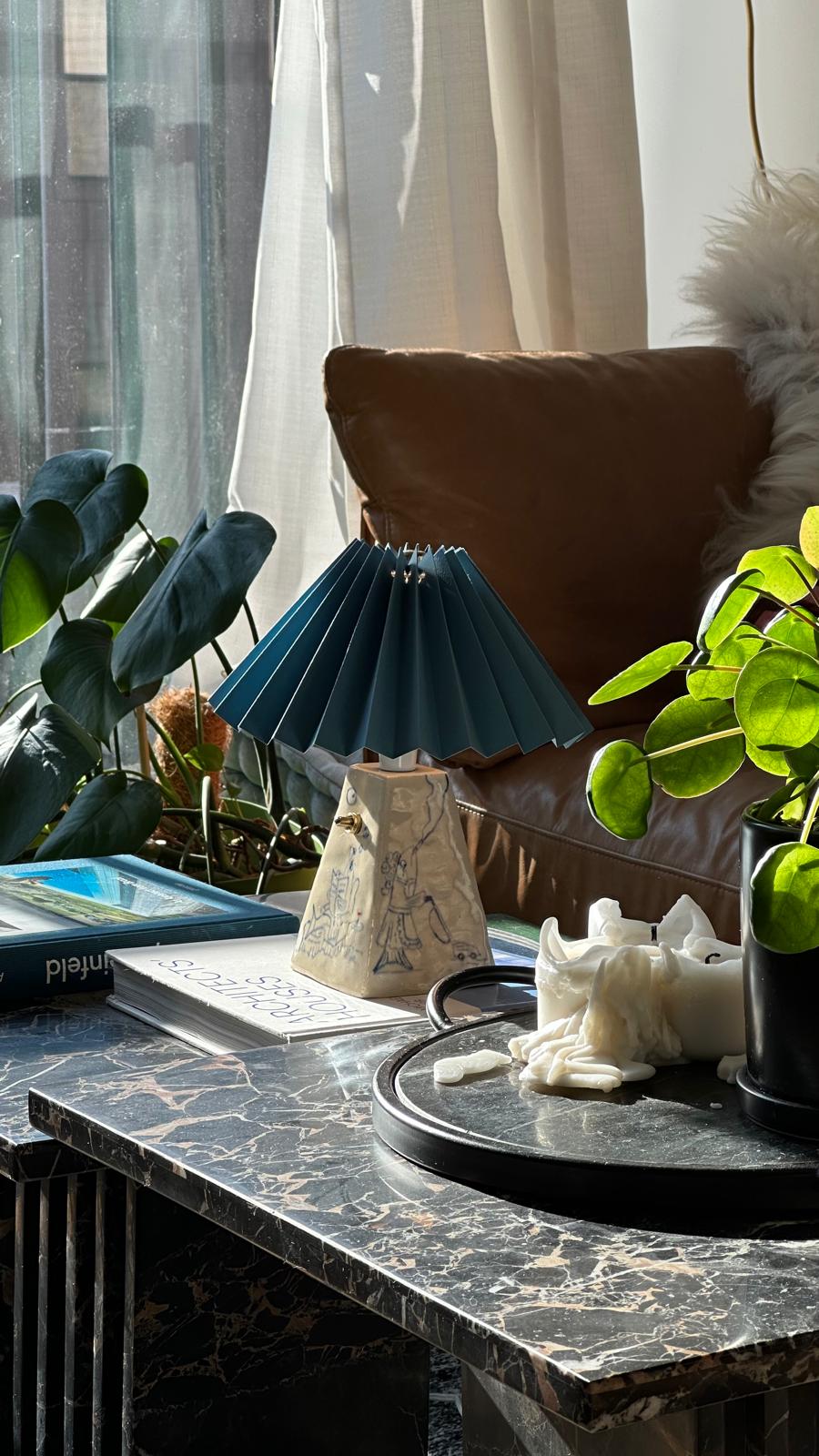 handcrafted ceramic lamp with pleated blue shade, on a coffee table in a brooklyn apartment