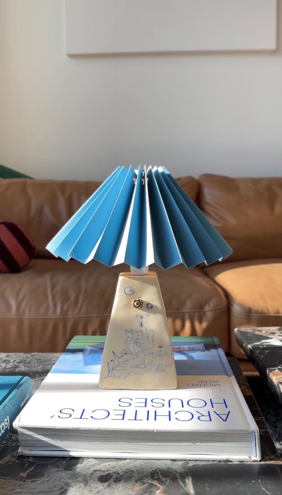 handmade ceramic lamp with an image of a Fish Dad lounging, with pleated blue shade on a coffee table