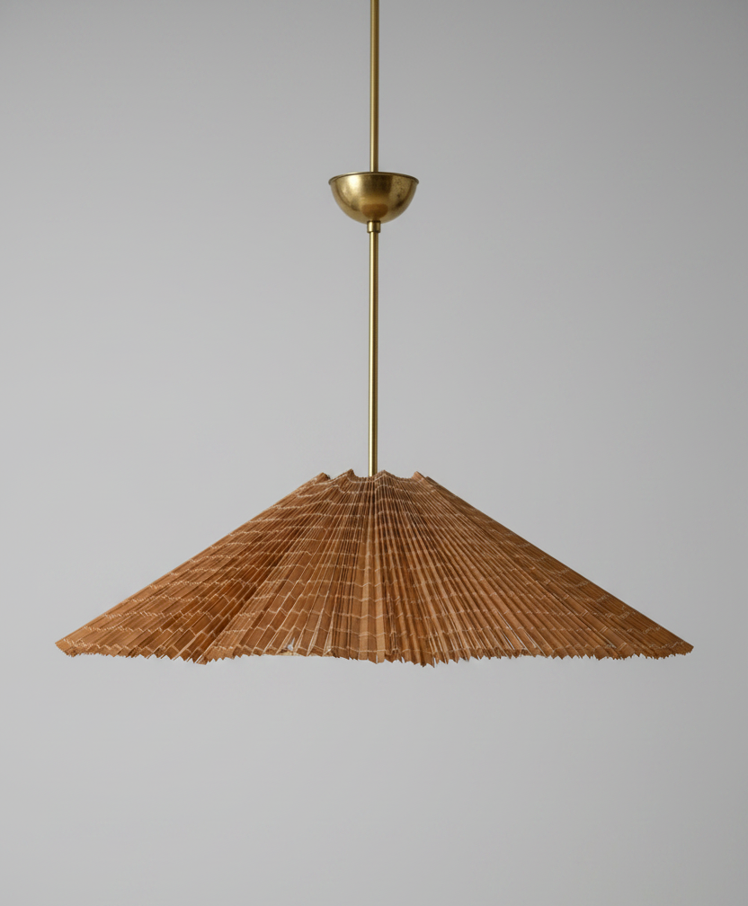 Pendant light with wicker shade and brass fixture on a gray background