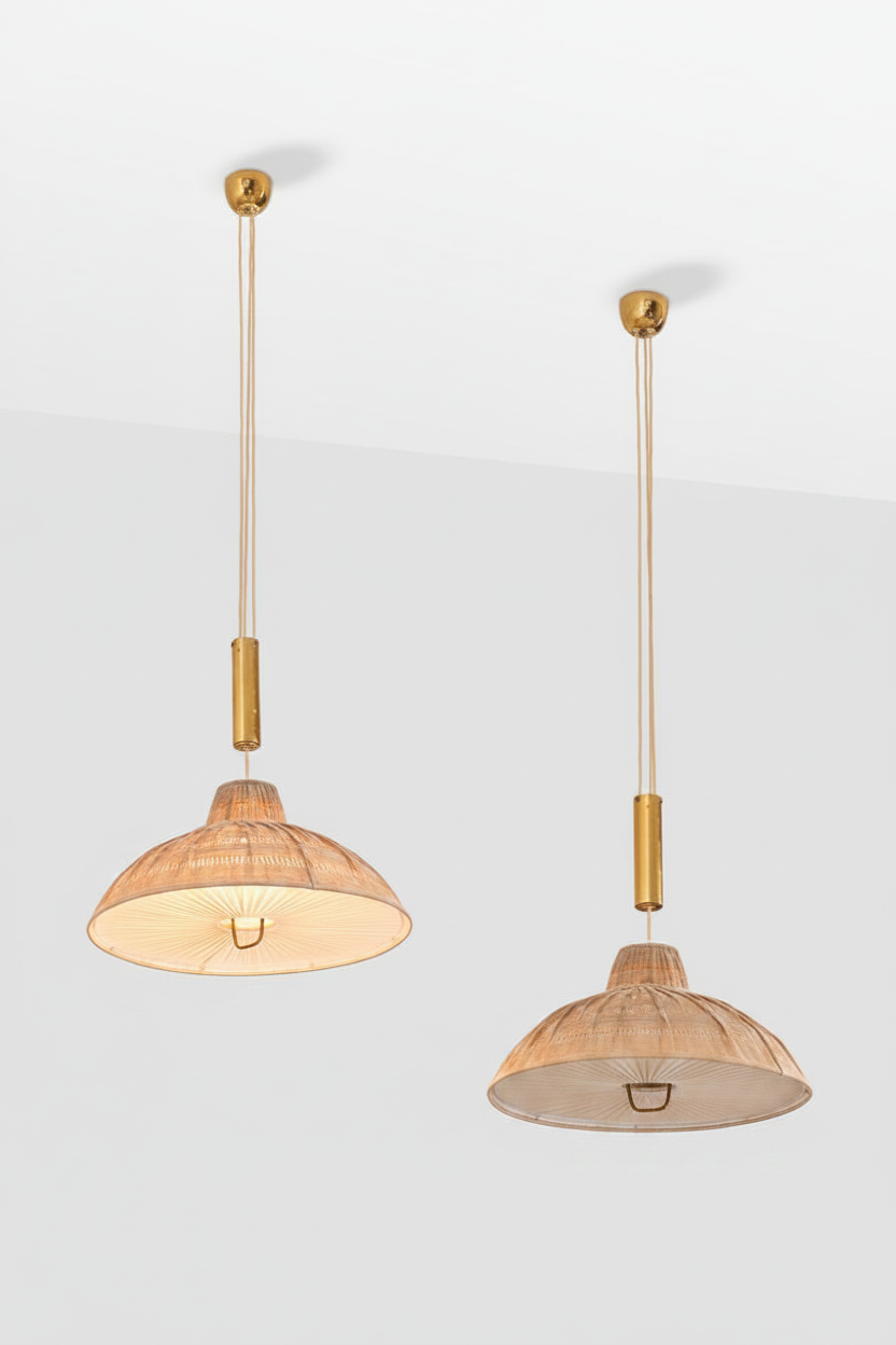 Two mid-century pendant lights with woven natural wood shades and brass hardware, suspended against a clean white wall. One is turned on, one is off.