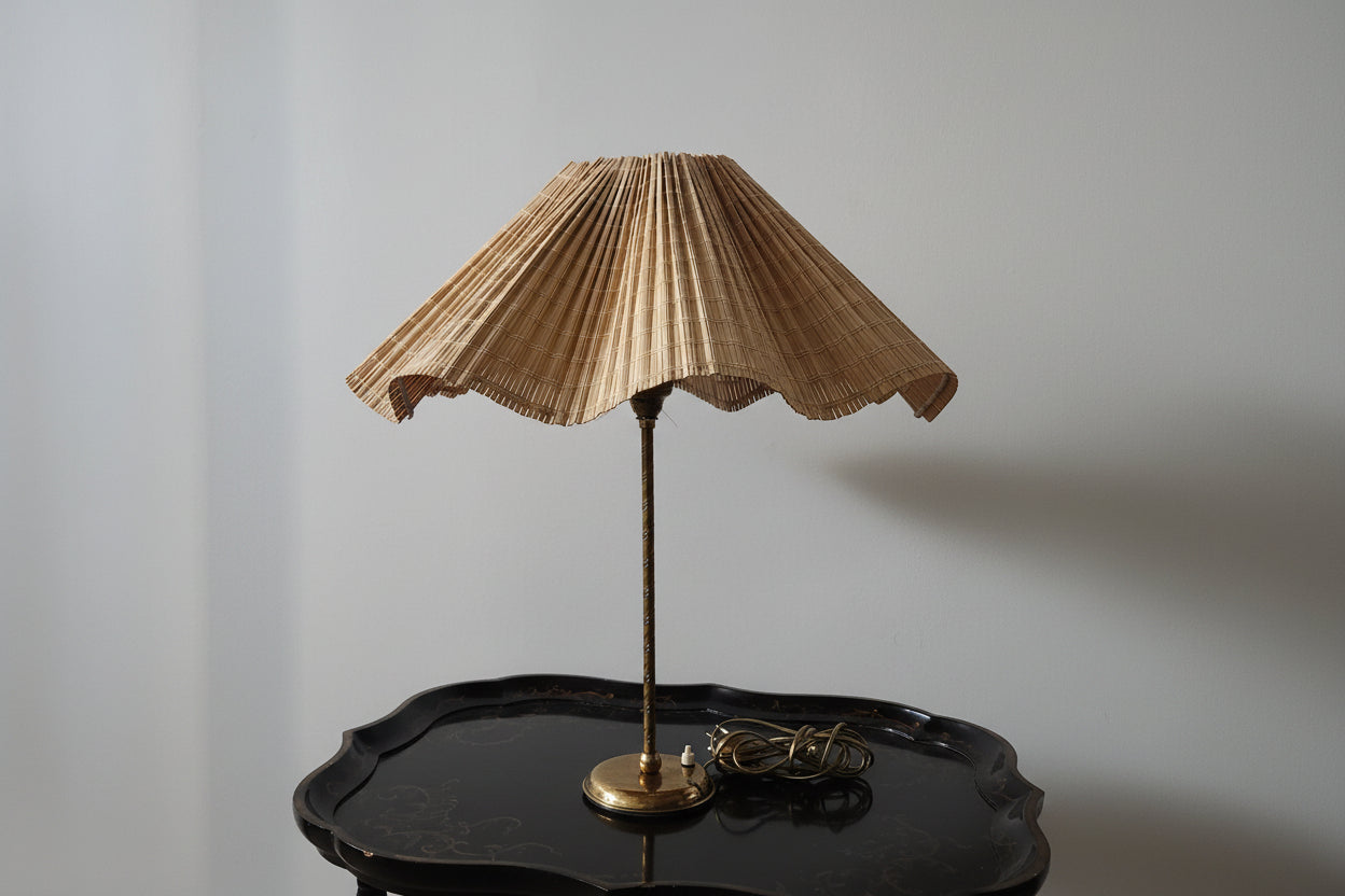 Vintage-style lamp with pleated shade on a dark wooden table against a plain wall.