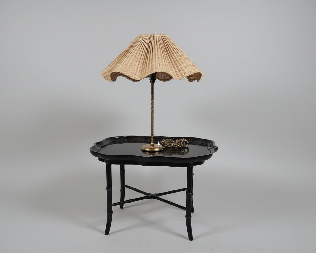 Table lamp with pleated shade on a black table against a white wall.