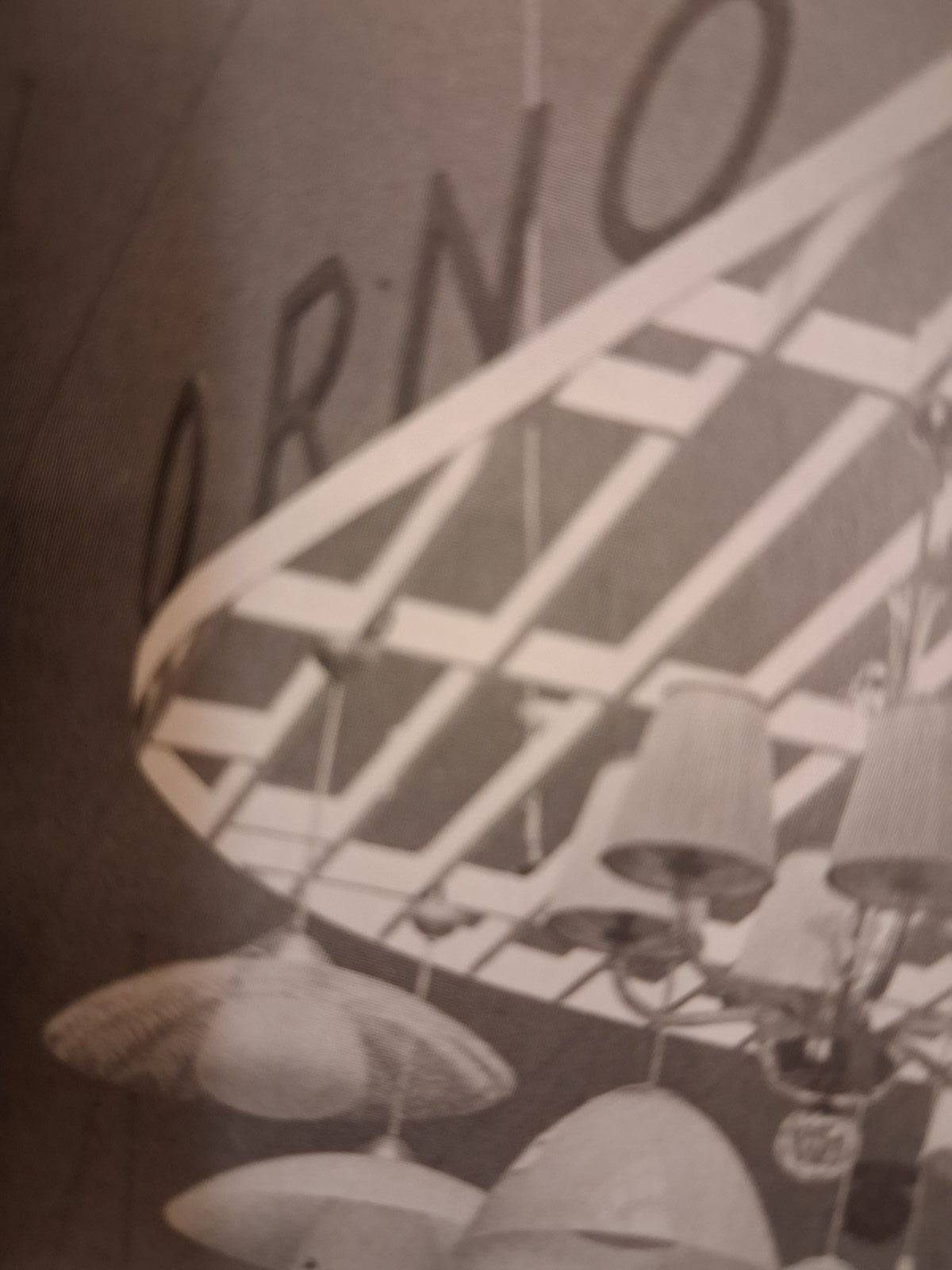A vintage black and white photograph showing a modern geometric ceiling light fixture with multiple hanging shades, set against a dark background with the letters 'ORNO' partially visible.