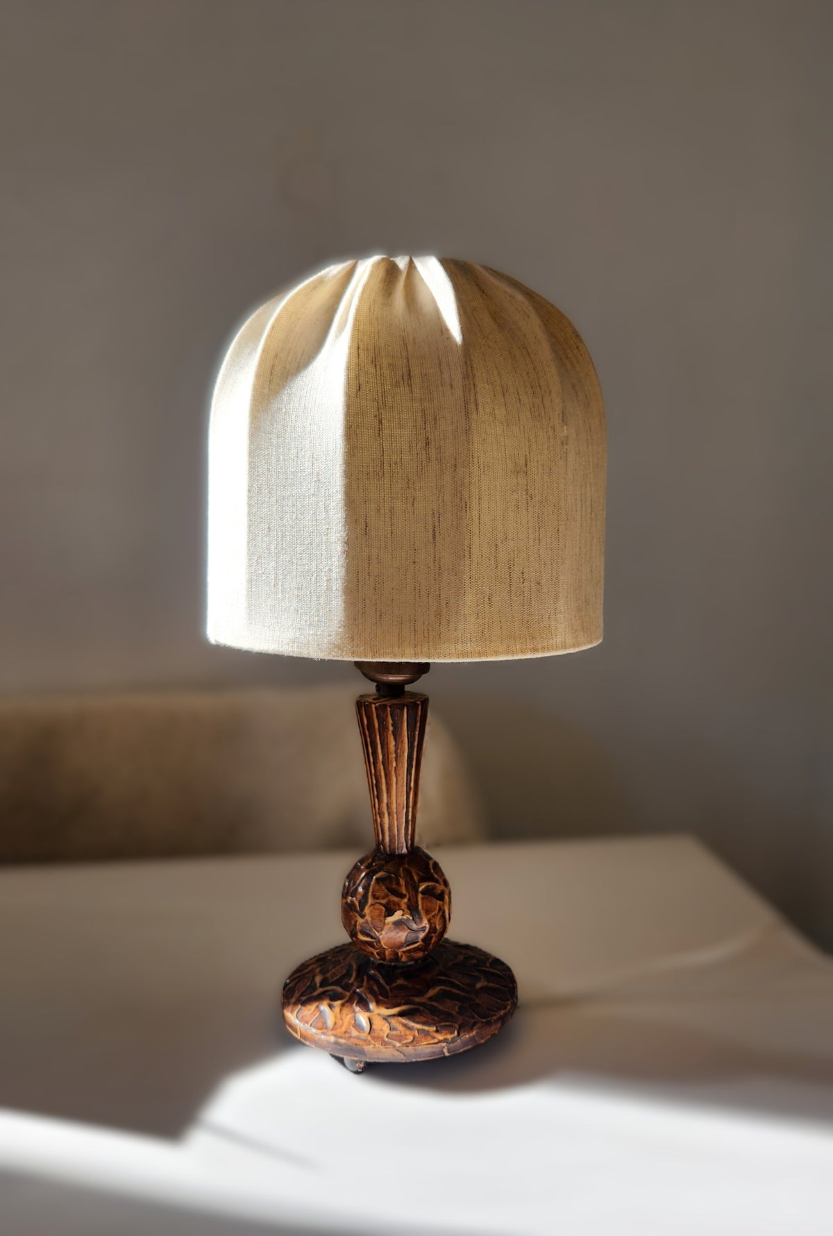 small vintage Swedish table lamp with wooden hand carved base and stem topped with a mushroom shaped linen lampshade, set on a white table