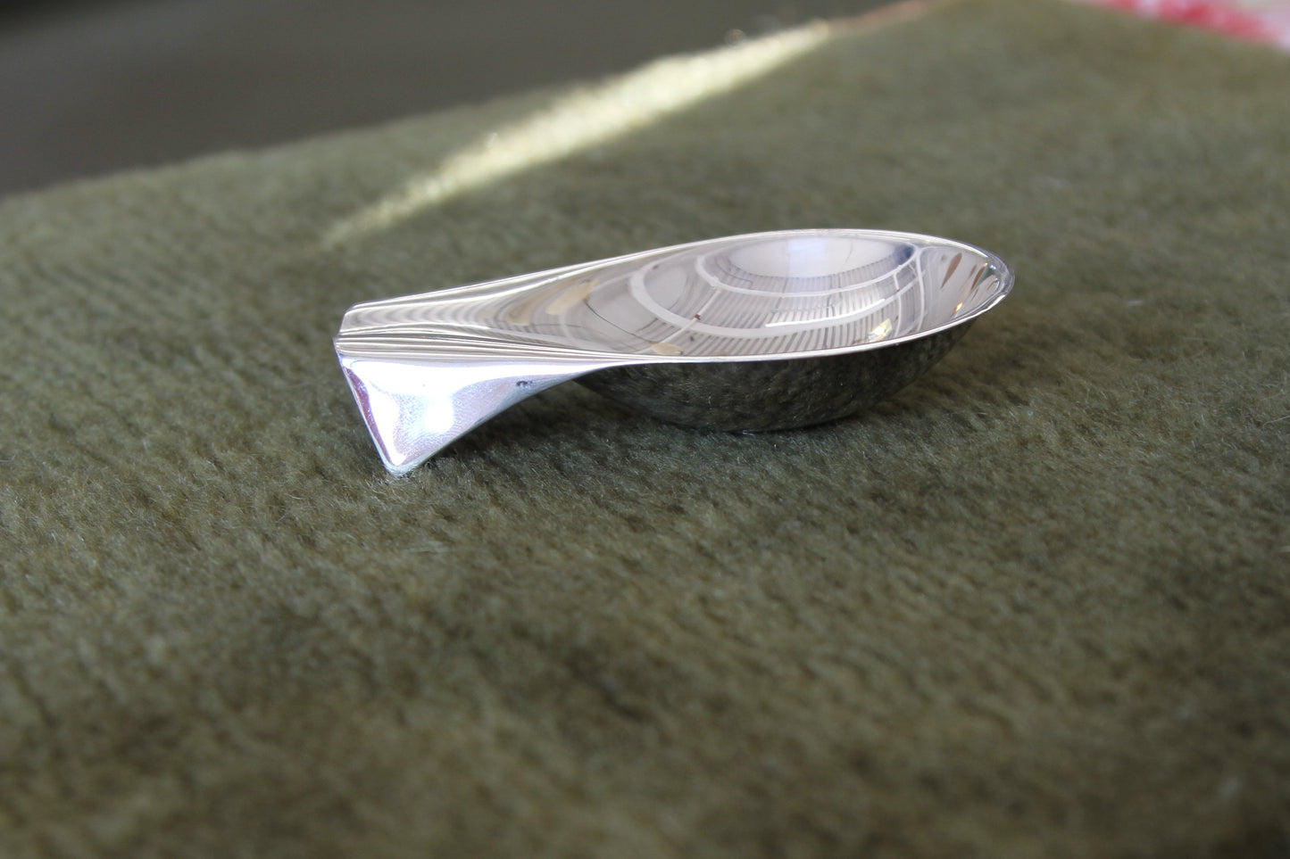Silver fish-shaped object on a green fabric surface