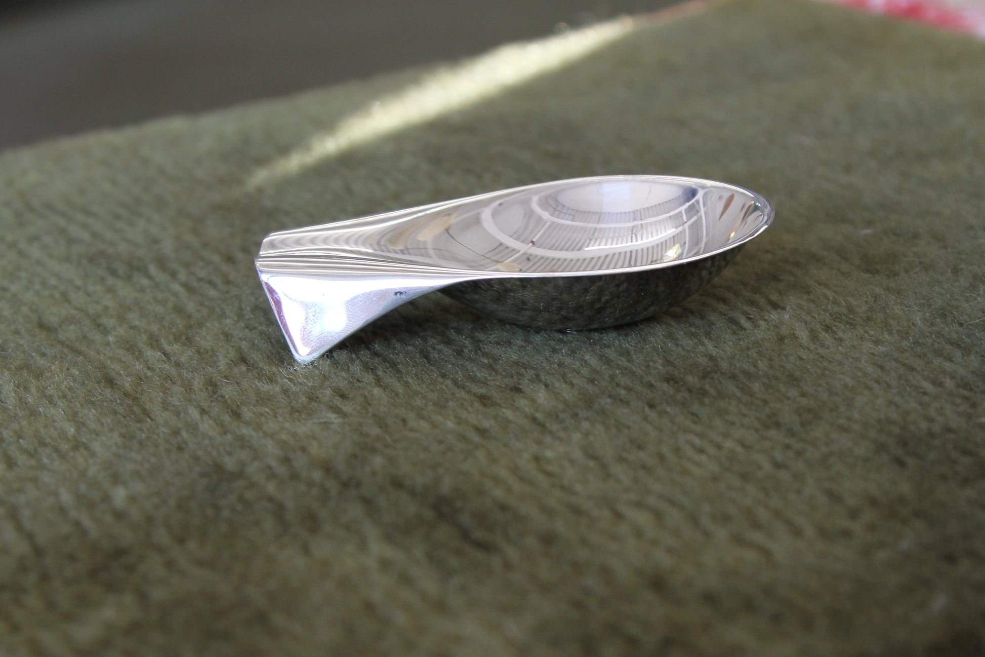 Silver fish-shaped object on a green fabric surface