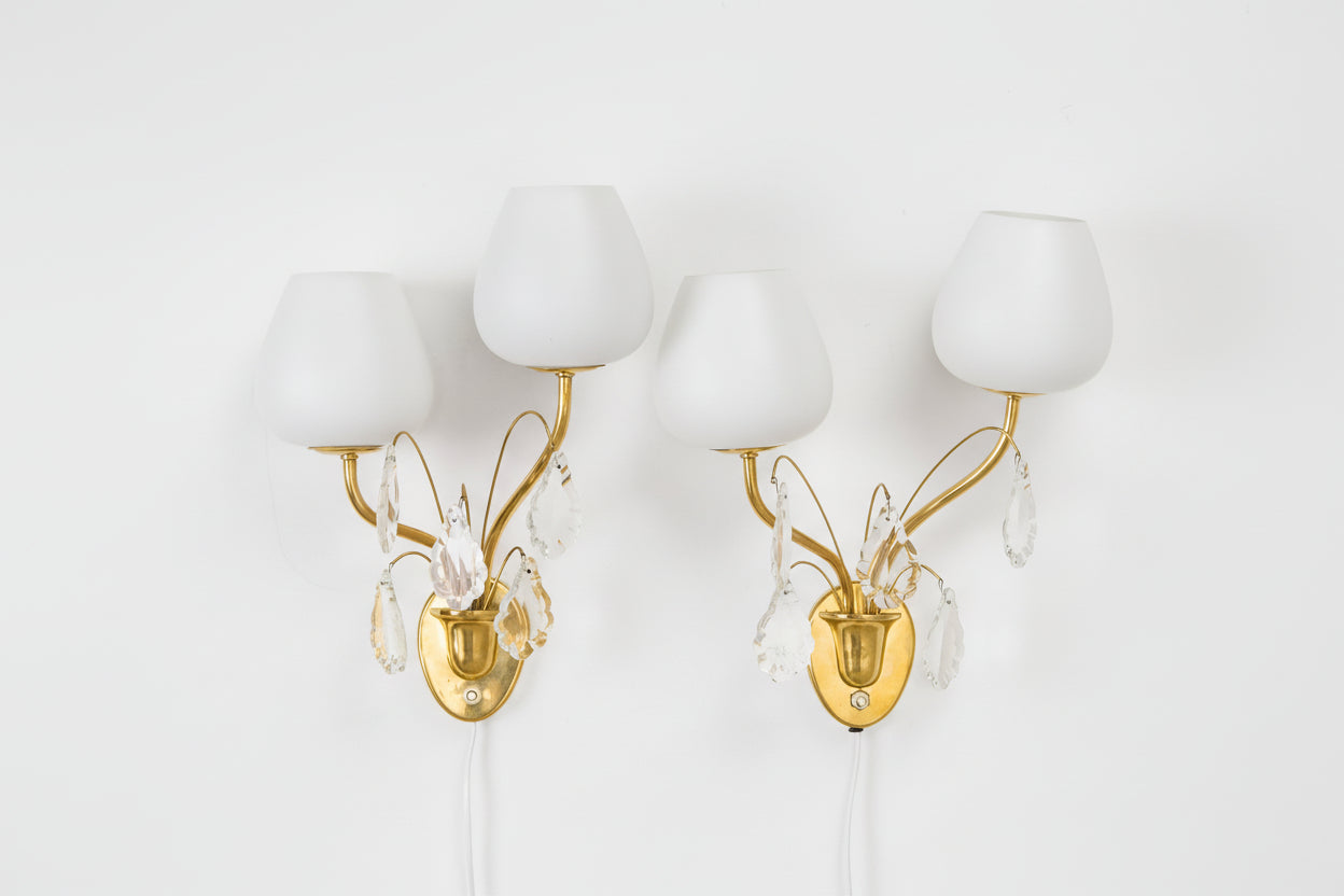 Pair of gold wall sconces with white glass shades on a light gray background