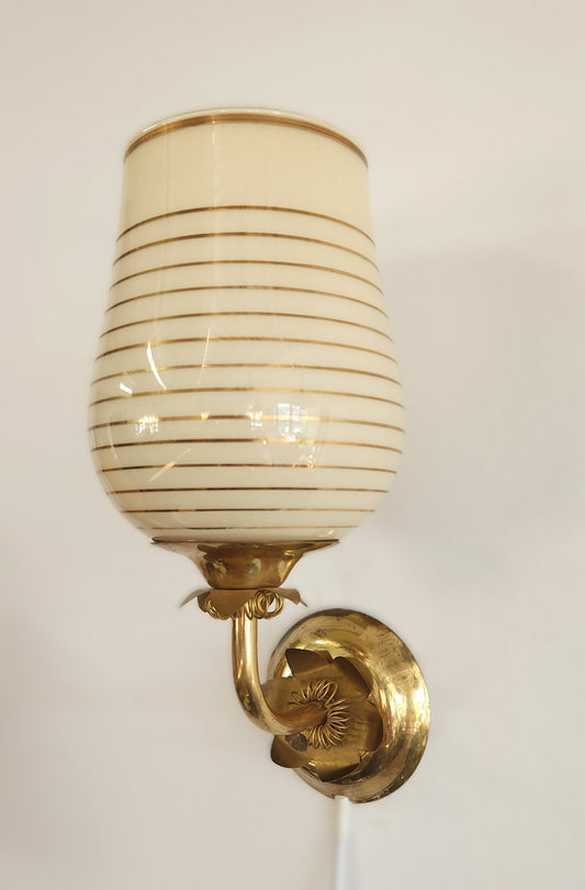 A vintage wall sconce with a cream-colored glass shade featuring horizontal gold stripes and a polished brass wall mount.