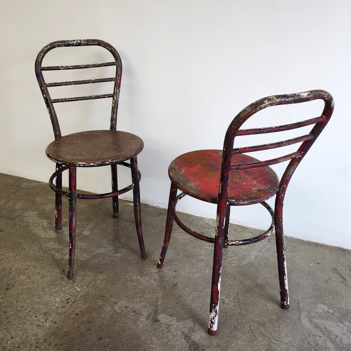 Two vintage metal chairs with different colors on a concrete floor against a white wall.